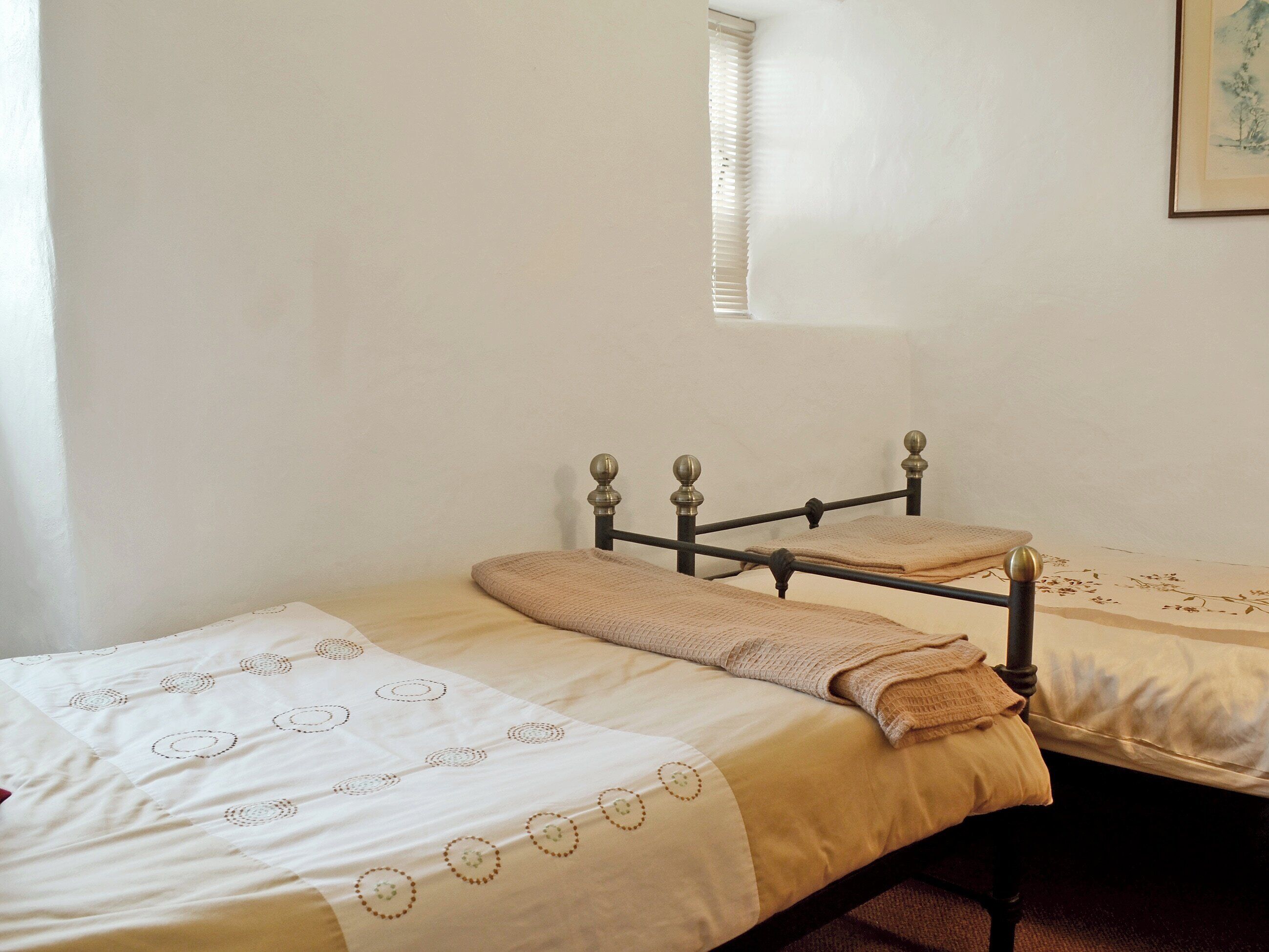 A single bed with a metal frame and a beige blanket.