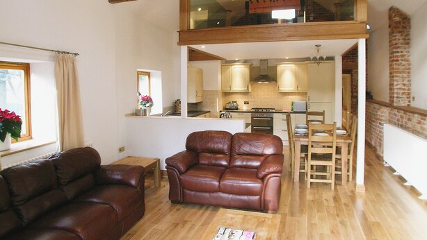 A spacious living area with a high ceiling, a dining table, and a kitchen in the background. - The Street Farm Barn (Costessey, Norwich)