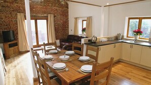 A dining area with a brick wall, wooden table, and chairs. - The Street Farm Barn (Costessey, Norwich)