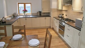 A kitchen with wooden cabinets, a stove, and a window with a view. - The Street Farm Barn (Costessey, Norwich)