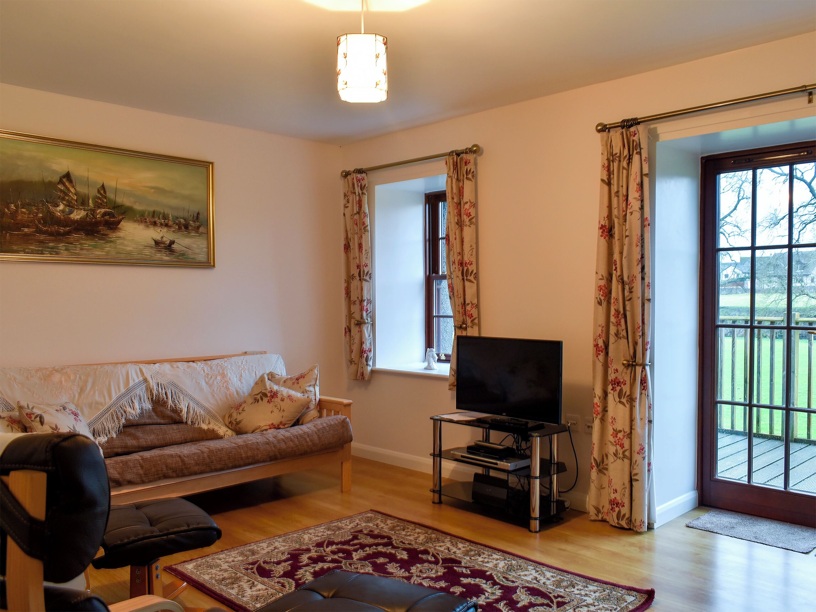 Una sala de estar con un sofá, un televisor sobre un mueble bajo, un cuadro en la pared y vistas a través de una ventana.