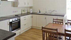Eine moderne Küche mit weißen Schränken, einem eingebauten Backofen, einer Edelstahl-Dunstabzugshaube, einem Spülbecken mit Geschirrgestell und einem Essbereich mit Holztisch und Stühlen.