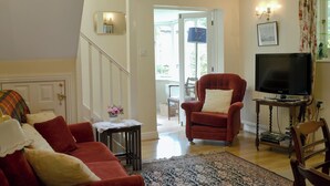 Un salon comprenant un canapé, un fauteuil, une télévision et une petite table avec une lampe.