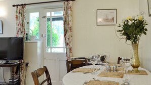 Un coin repas avec une table dressée pour deux personnes, un téléviseur et un tableau encadré au mur.
