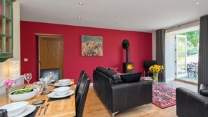 Een moderne woonkamer met een rode muur, een open haard, een eethoek met een tafel gedekt voor twee personen en een bank.