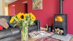 Een woonkamer met een bank, een glazen salontafel met een vaas zonnebloemen, een open haard en een rode muur met een schilderij.