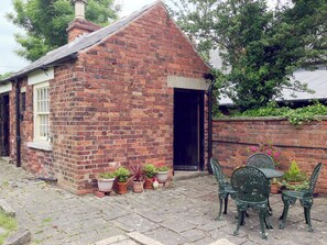A brick cottage with a tiled roof, a small porch with potted plants, and a table and chairs set up outside. - Jug And Glass Cottage (Nether Langwith, near Mansfield)