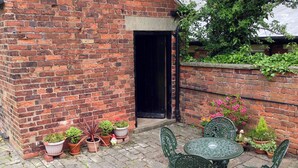 A brick building with a black door, potted plants, and a green metal table and chairs.