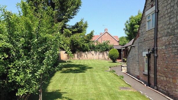 A well-maintained lawn with a stone building on the right and a brick house in the background.