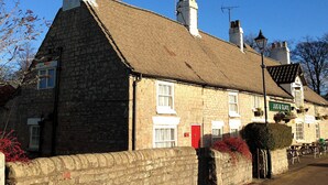 A stone building with a thatched roof, a red door, and a sign reading "JUG & GLASS".