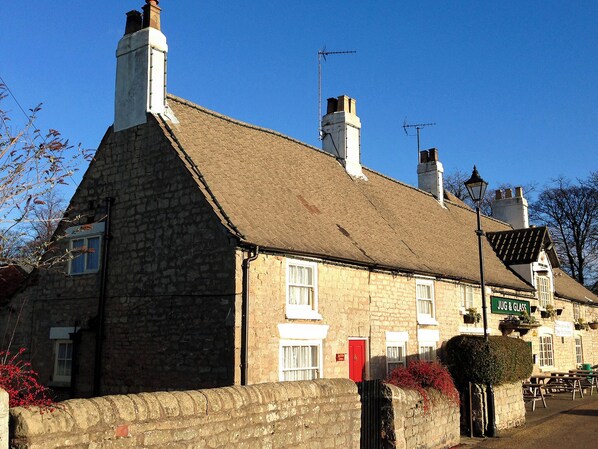 A stone building with a thatched roof, a red door, and a sign reading "JUG & GLASS". - Jug And Glass Cottage (Nether Langwith, near Mansfield)