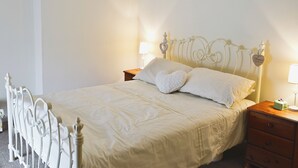 A neatly made bed with a white headboard and footboard, a wooden nightstand with a lamp, and a small bedside table with a decorative item.