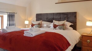 A neatly made bed with a red blanket, two pillows with animal designs, a wooden nightstand with a lamp, and a window with a curtain. - All on the Ground Floor: 
Open plan living space. (near Kirkbymoorside)