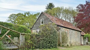Une maison de campagne en pierre, dotée d’un toit en pente, entourée d’un jardin et de constructions en bois.