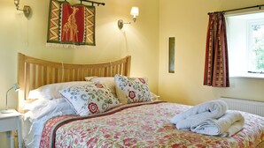Un lit bien fait, avec une literie à motifs floraux, une tête de lit et deux lampes fixées au mur.