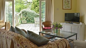Un salon comprenant un canapé, une table basse en verre, un téléviseur et une vue sur un jardin, accessible par une porte-fenêtre coulissante.