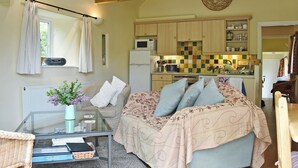 Une pièce confortable avec un lit, une table en verre sur laquelle sont posés des livres, un radiateur et un coin cuisine doté de meubles en bois et d’un four à micro-ondes.