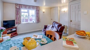 A cozy living room with a leather sofa, a television, a dining table with a book, a teapot, and a bowl of cookies. - 1 bedroom accommodation in Goldsborough, near Harrogate (Goldsborough, near Harrogate)
