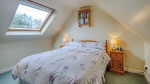 A bedroom with a skylight, a bed with floral bedding, bedside lamps, a wooden nightstand, and a bookshelf. - 1 bedroom accommodation in Goldsborough, near Harrogate (Goldsborough, near Harrogate)