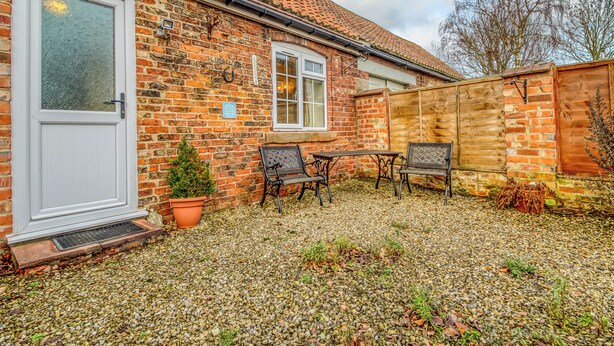 A brick house with a tiled roof, a white door, and a small patio area with a table and chairs. - 1 bedroom accommodation in Goldsborough, near Harrogate (Goldsborough, near Harrogate)