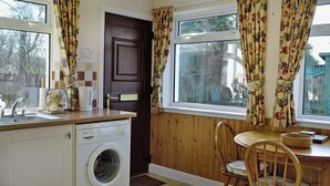 A compact kitchen with a washing machine, a sink, and a dining area with a chair and table. - 2 bedroom accommodation in Benderloch near Oban (Benderloch near Oban)