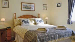 A neatly made bed with a plaid blanket, two pillows with dog prints, and a bedside lamp. - 2 bedroom accommodation in Benderloch near Oban (Benderloch near Oban)