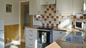 A compact kitchen with white cabinets, a tiled backsplash, a toaster, a microwave, a sink, and a stove. - 2 bedroom accommodation in Benderloch near Oban (Benderloch near Oban)