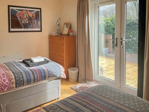 A bedroom with a bed, a dresser, a framed artwork, a desk with a lamp, and a sliding glass door to a patio.