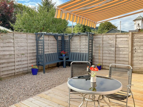 A patio area with a round table and chairs, a bench, and a pergola with a striped awning. - 1 bedroom accommodation in Drumnadrochit (Drumnadrochit)