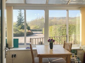 A room with a table and chairs, a window with a view of a garden and trees, and a power outlet on the wall.
