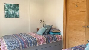 Een slaapkamer met twee bedden, een houten deur en een aan de muur bevestigd boslandschap.