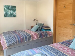 A bedroom with two beds, a wooden door, and a wall-mounted picture of a forest. - 1 bedroom accommodation in Drumnadrochit (Drumnadrochit)