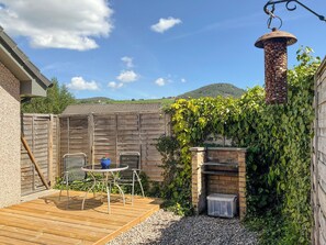 A patio with a wooden deck, a metal table and chairs, a brick fireplace, and a hanging bird feeder.