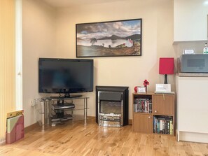 A living room with a flat-screen TV, a fireplace, a bookshelf, and a framed landscape painting on the wall. - 1 bedroom accommodation in Drumnadrochit (Drumnadrochit)