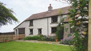 A white stone house with a tiled roof, a wooden fence, and a well-maintained lawn.