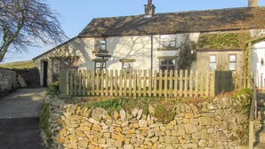 A stone wall with a wooden fence in front of a house with multiple windows and a chimney.