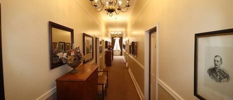 A hallway with a chandelier, framed pictures, and a wooden dresser with a vase of flowers.