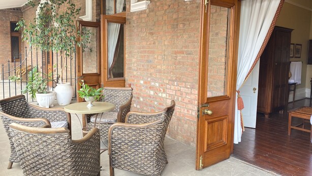 Un espace extérieur accueillant, aménagé avec des chaises et une table en osier, entouré de murs en briques et de grandes fenêtres.