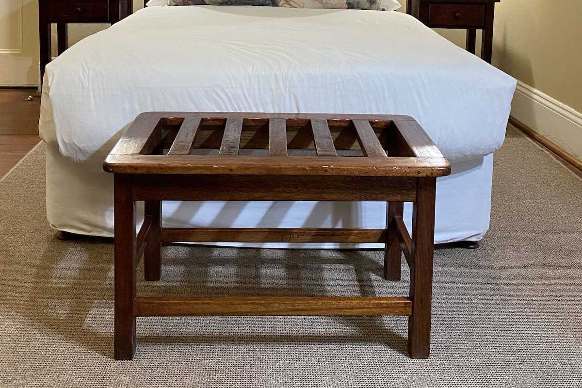 Un lit bien fait, avec une tête de lit en bois, deux tables de chevet avec des lampes, un tableau encadré au mur et une petite plante sur l’une des tables.