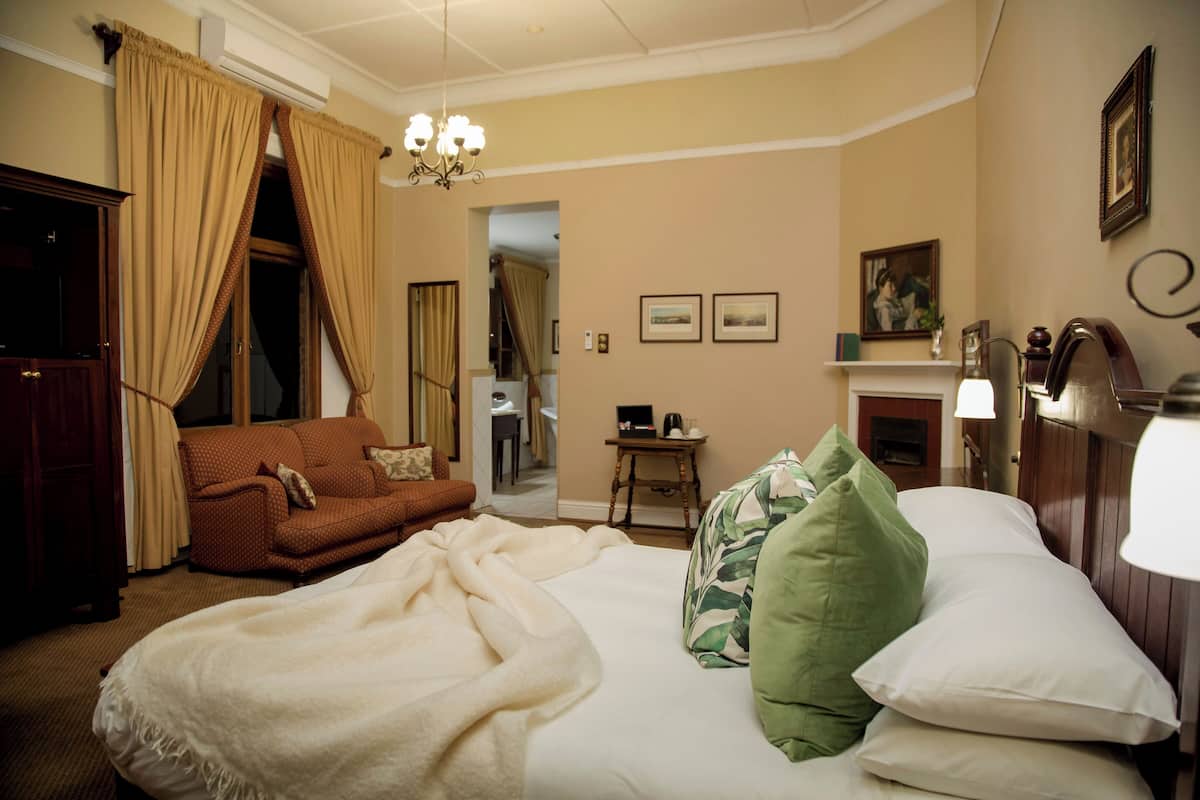 Une chambre d’hôtel avec un lit, un canapé, un lustre, une cheminée et des tableaux encadrés accrochés au mur.