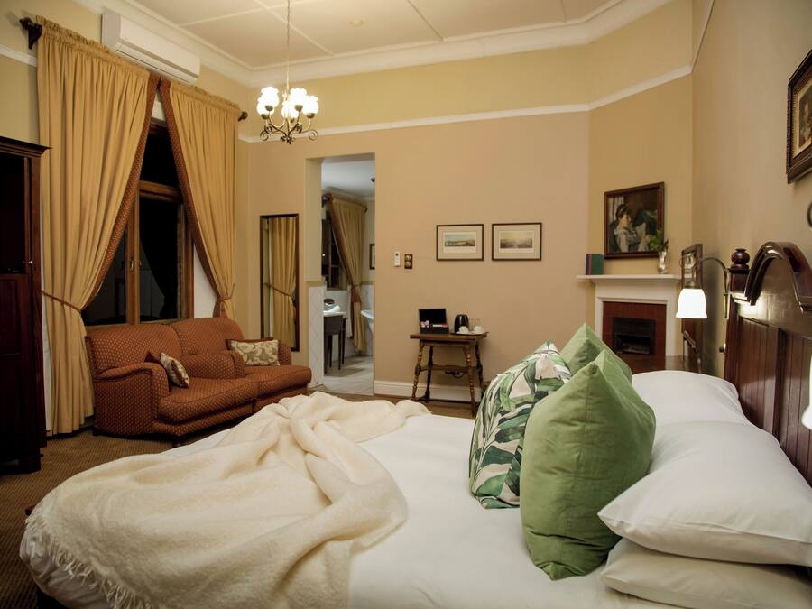 A hotel room with a bed, a sofa, a chandelier, a fireplace, and framed pictures on the wall.