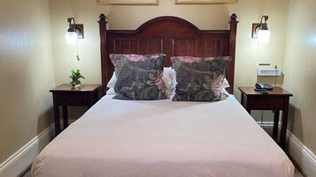 Habitación de hotel con una cama grande, dos mesitas de noche, un banco de madera y dos cuadros en la pared.