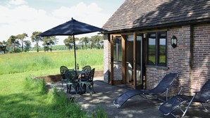Una casa de ladrillo con un patio que incluye una mesa, sillas, una sombrilla y dos sillones.