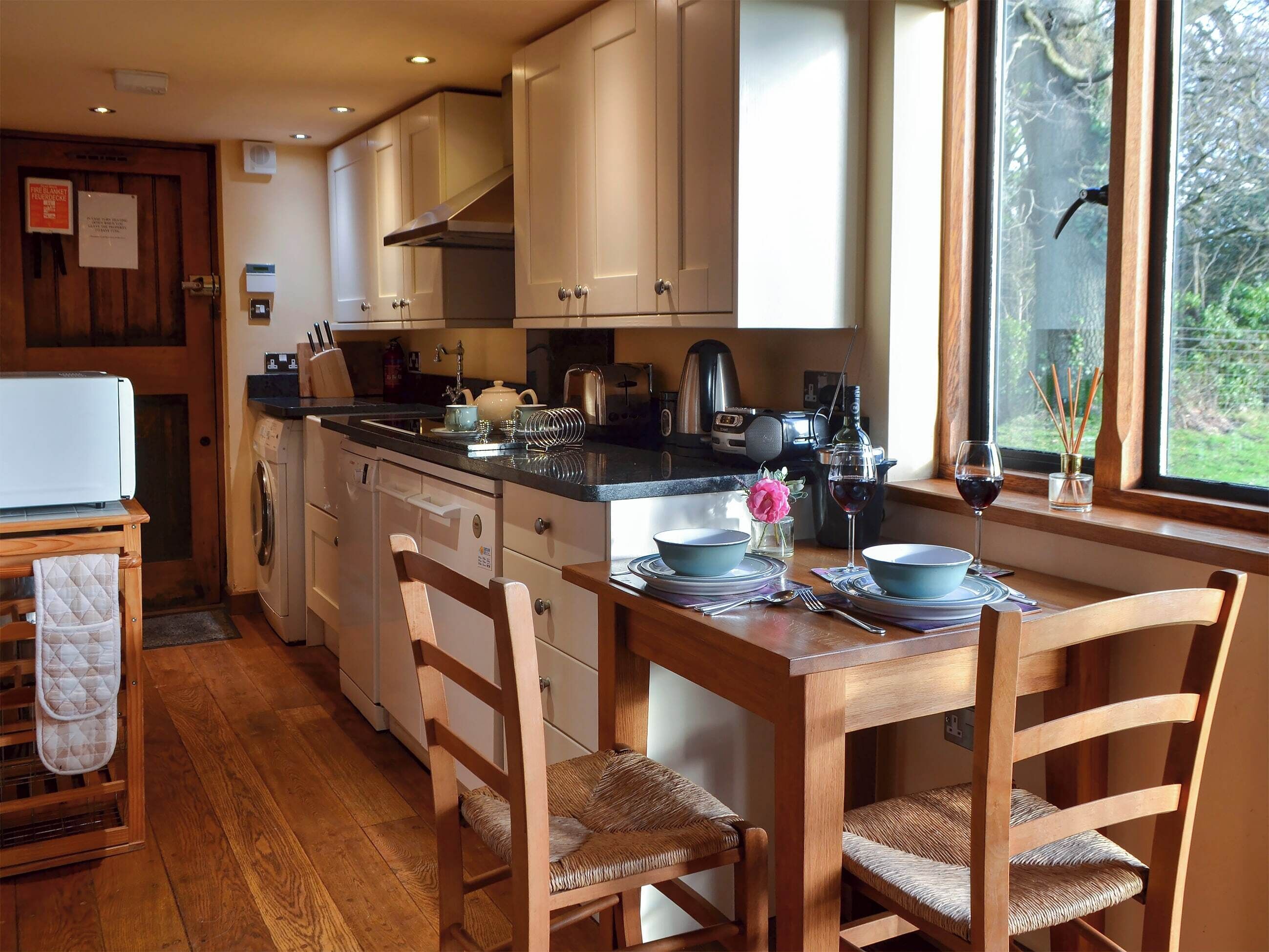 A kitchen with wooden cabinets, a dining table set for four, and a view of the outdoors through a window.