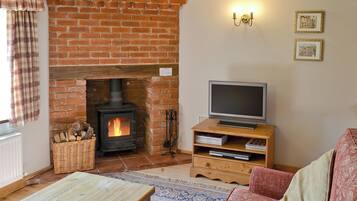 A cozy living room with a brick fireplace, a television on a wooden stand, and a patterned rug.