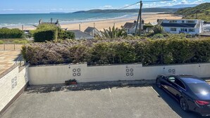 Vista costera con playa, casas y un coche aparcado.