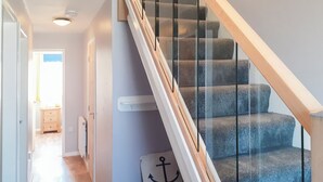 Una escalera con barandillas de vidrio y peldaños de madera que conduce a una habitación con una puerta y una mesita.