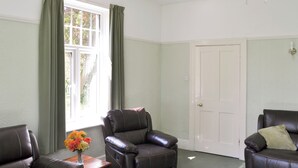 A living room with two leather sofas, a wooden coffee table, and a vase of flowers. A white door is visible in the background. - 3 bedroom accommodation in Waxham (Waxham)