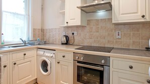A modern kitchen with white cabinetry, a built-in washing machine, an oven, and a kettle on the countertop. - 3 bedroom accommodation in Waxham (Waxham)
