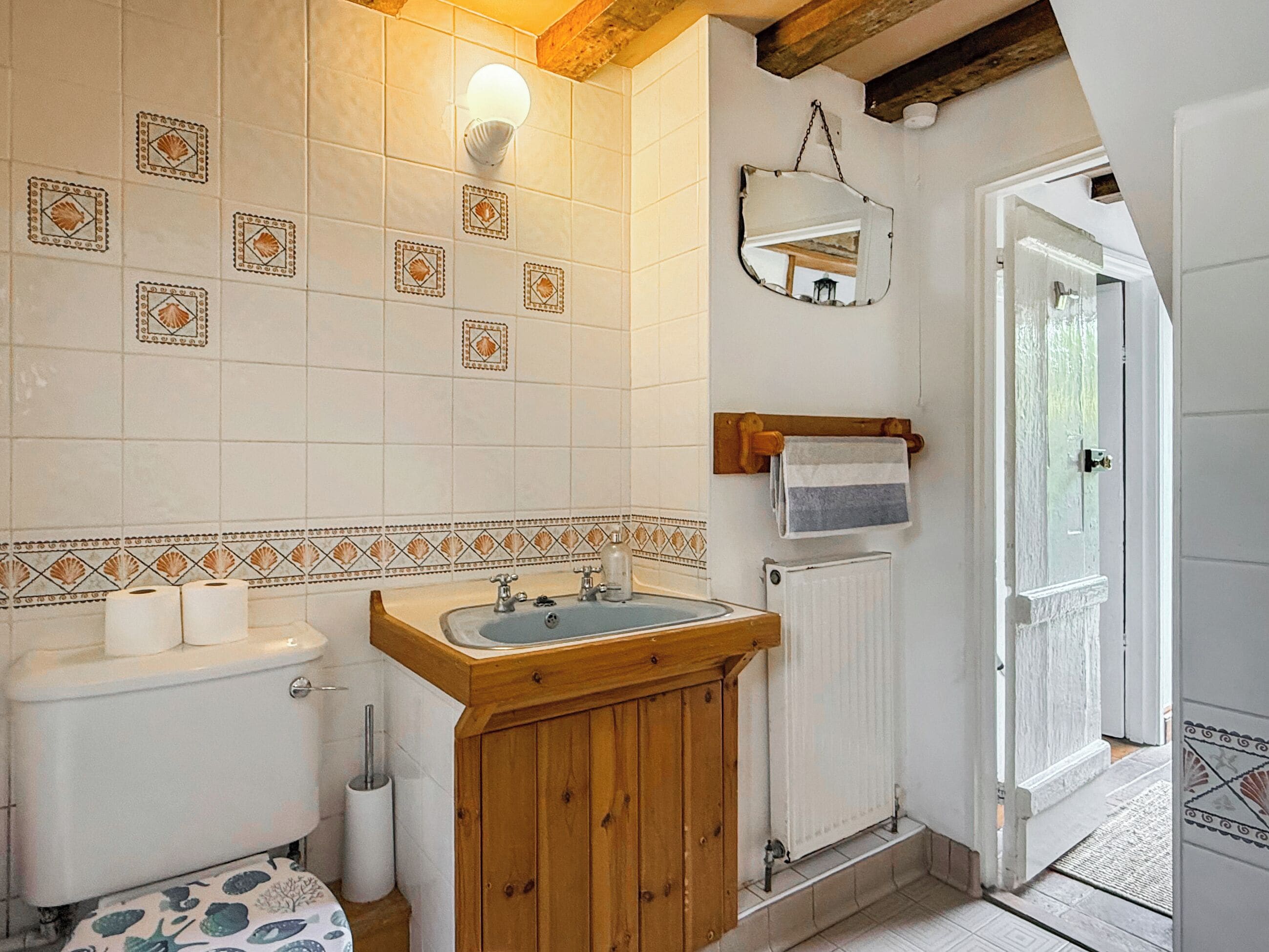 A bathroom with a toilet, sink, and mirror. There is a towel rack with a towel hanging on it. The walls have decorative tiles.